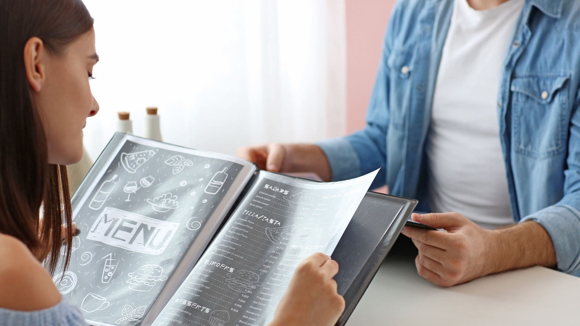 Guests reviewing a restaurant menu at the table while deciding what to order before a meal.