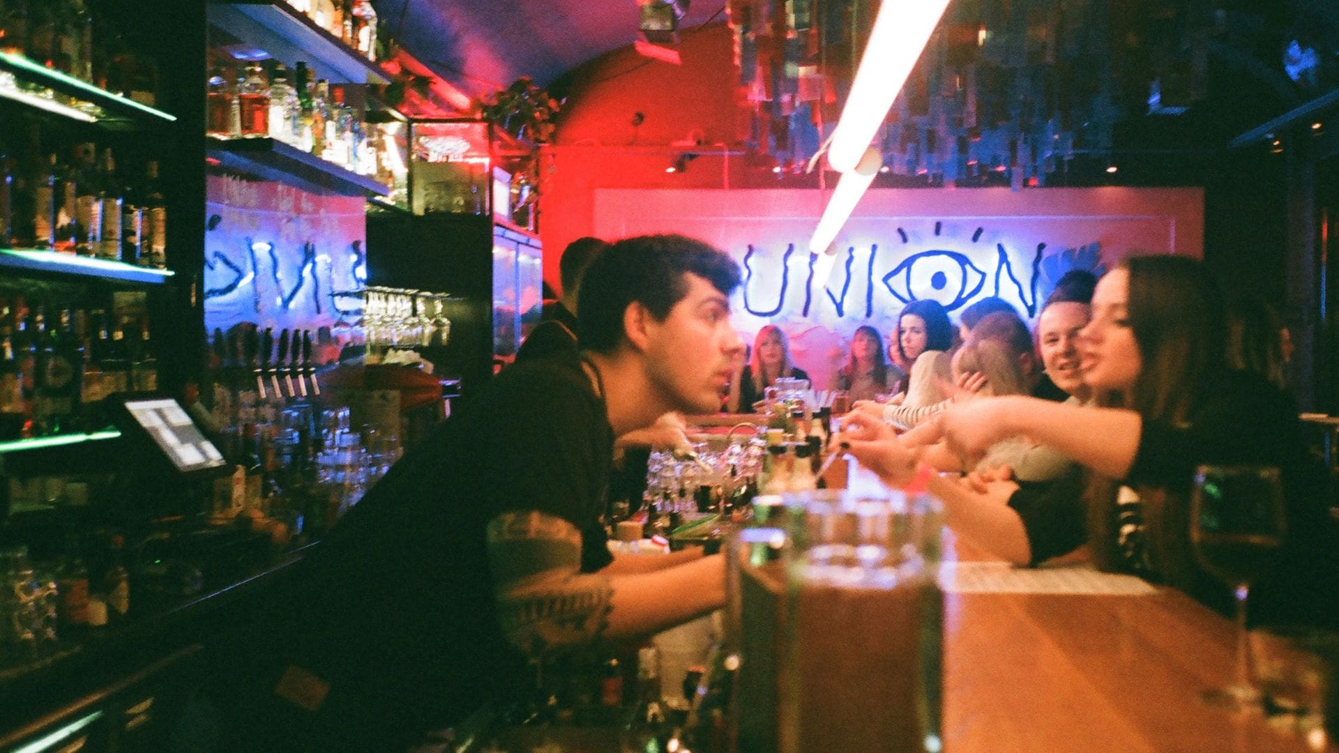 Guests gathered at a lively cocktail bar with bartenders serving drinks during a busy open bar service.